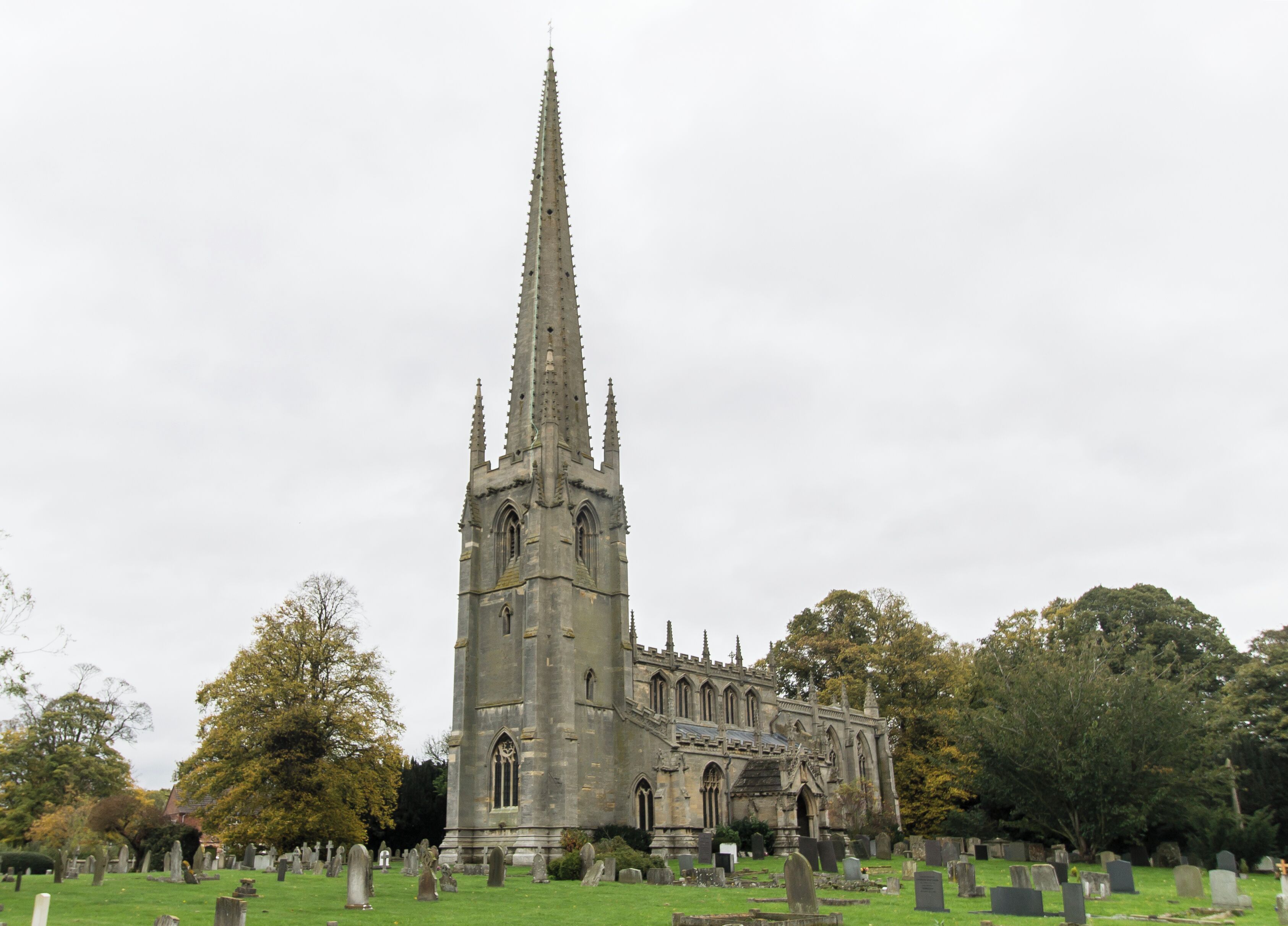 A Gothic church with a tall spire, surrounded by a cemetery with numerous headstones.