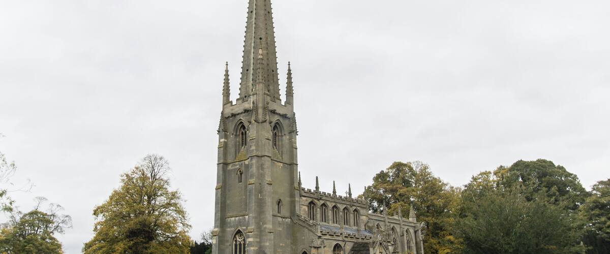 A Gothic church with a tall spire, surrounded by a cemetery with numerous headstones.