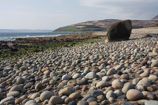 A pebble beach with large stones and a large boulder in the distance.