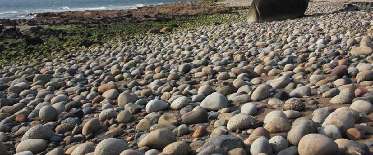 A pebble beach with large stones and a large boulder in the distance.