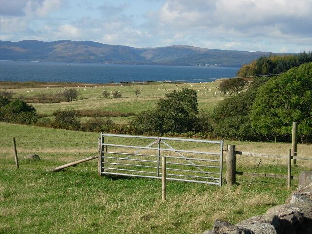 A rural landscape with a metal gate, grassy fields, and a body of water in the distance.