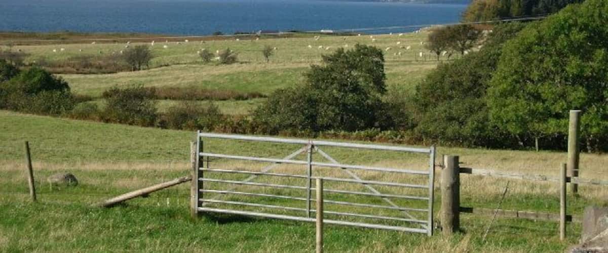 A rural landscape with a metal gate, grassy fields, and a body of water in the distance.