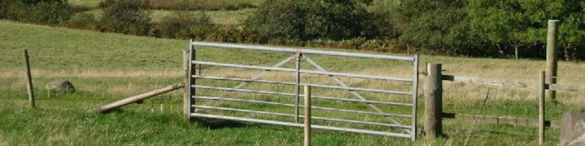 A rural landscape with a metal gate, grassy fields, and a body of water in the distance.