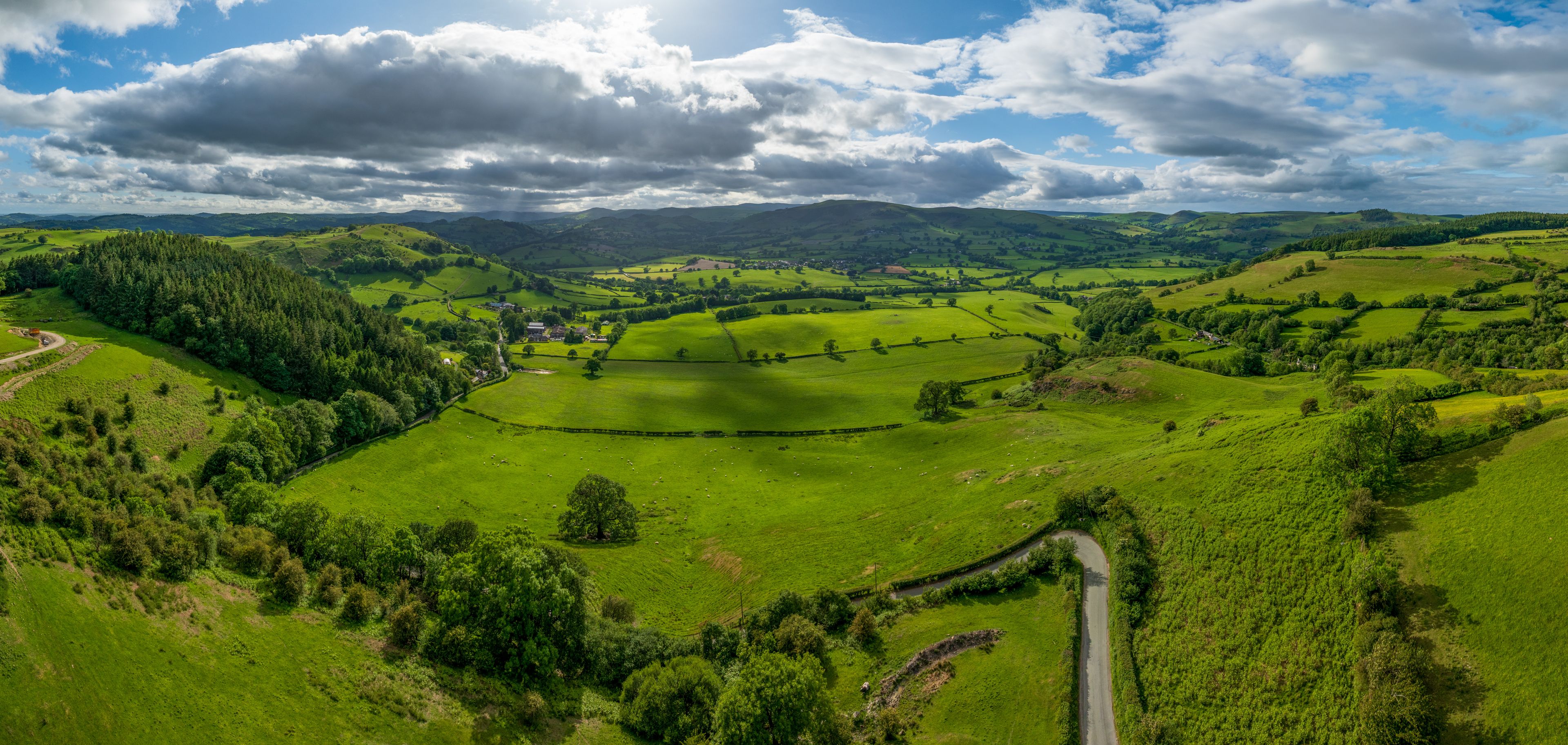 A lush green valley with rolling hills, a winding road, and a small village nestled among the fields.