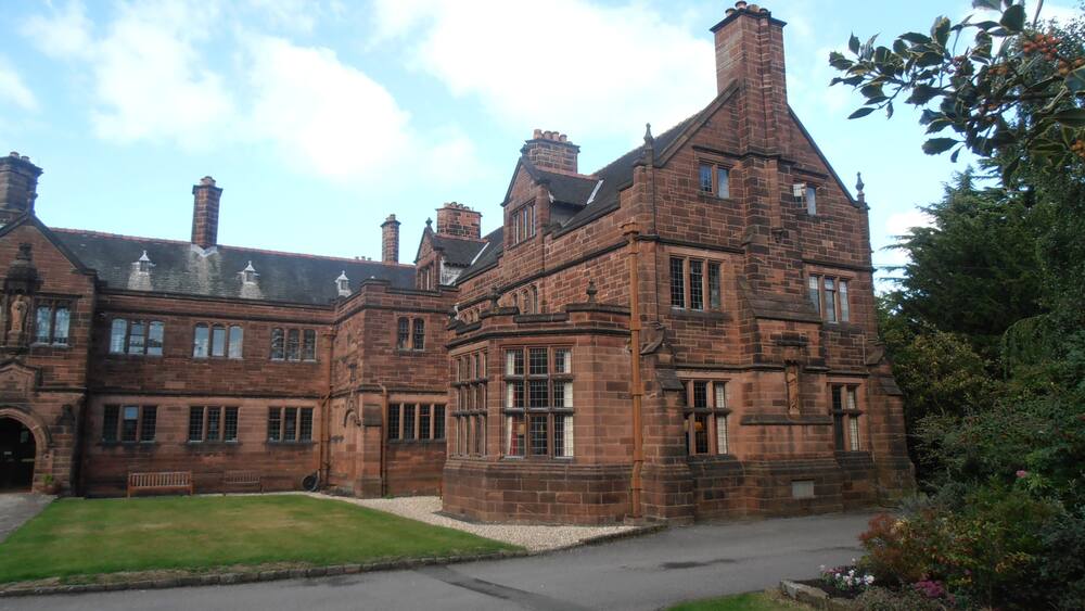 A large, historic brick building with multiple chimneys and a well-maintained lawn.