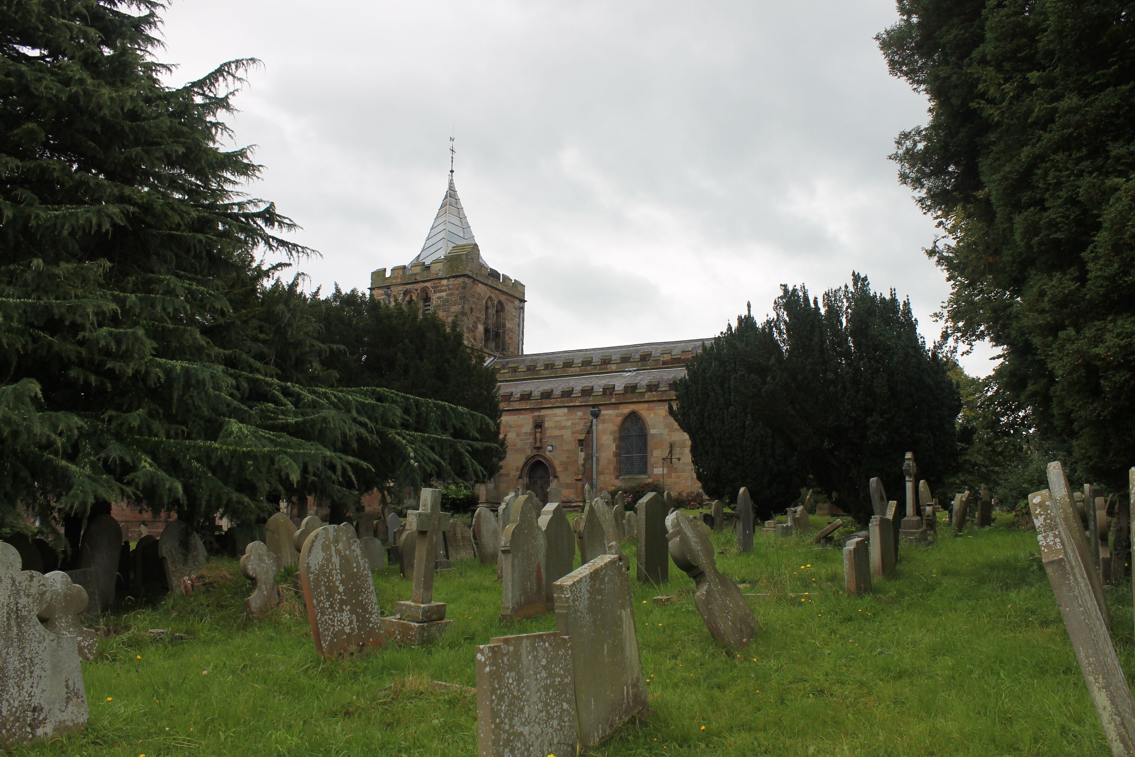 A cemetery with numerous headstones and a church with a pointed steeple in the background.