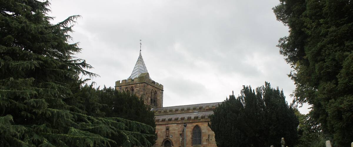 A cemetery with numerous headstones and a church with a pointed steeple in the background.
