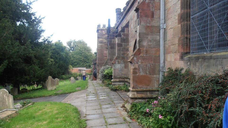 A stone pathway leading to a historic building with a metal fence and a cemetery in the background.