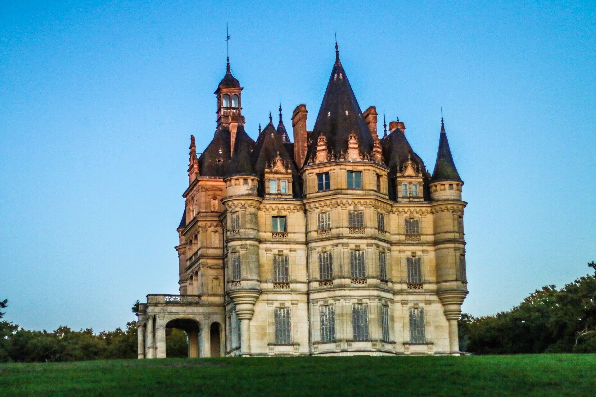 A large, historic castle with multiple towers and turrets, surrounded by a green landscape.