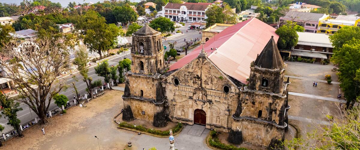 An old church with a red roof and two towers, surrounded by trees and buildings.