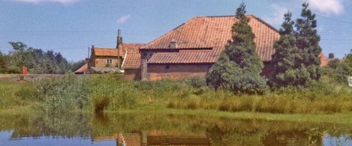 A house with a red roof, surrounded by trees and a body of water reflecting the structure.