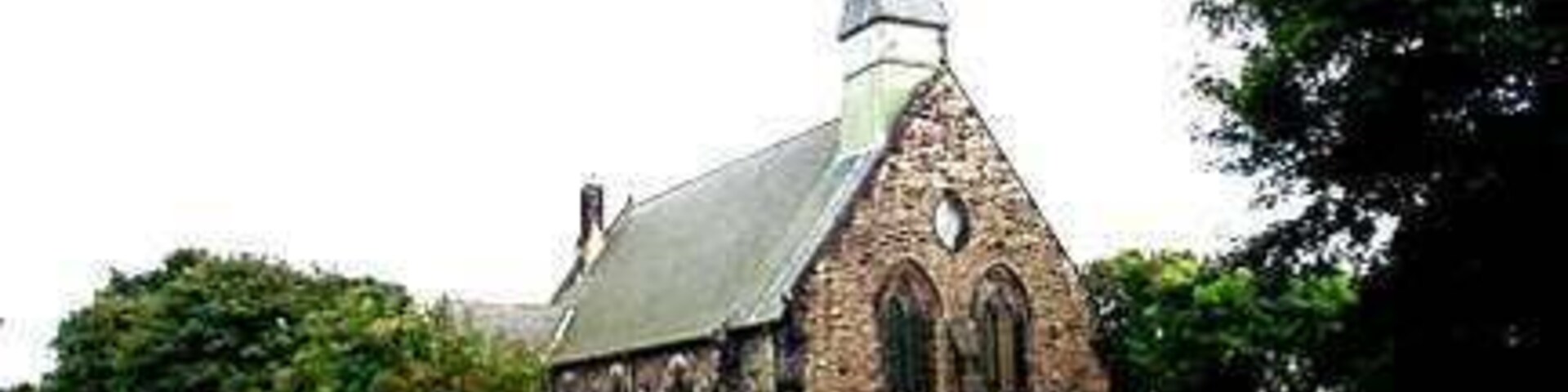 Una iglesia con un campanario puntiagudo y muros de piedra, rodeada por un cementerio con lápidas.