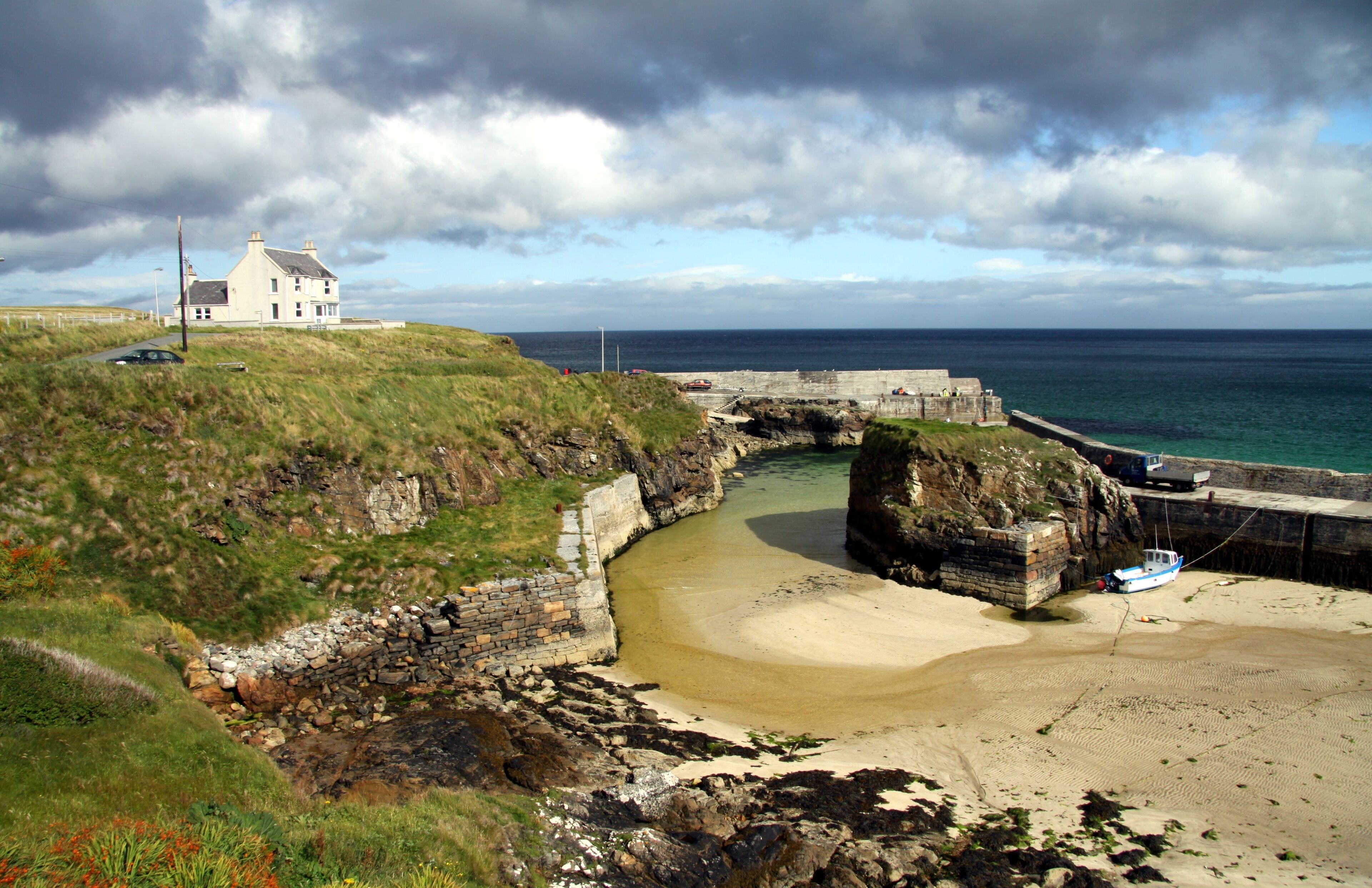 A coastal landscape with a white house, a stone bridge, and a sandy beach.