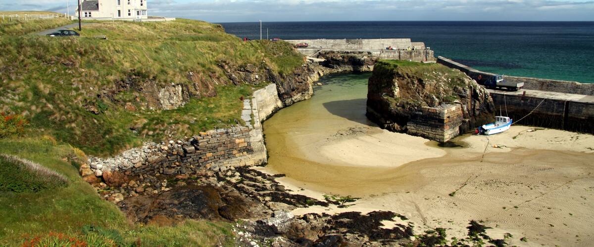 A coastal landscape with a white house, a stone bridge, and a sandy beach.