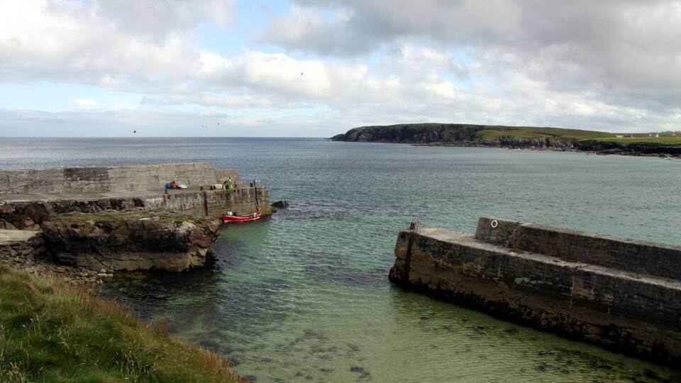 A coastal scene with a rocky breakwater, calm sea, and distant cliffs.