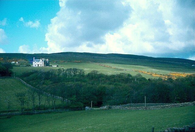 Una casa blanca sobre una colina con campos verdes y un muro de piedra al frente.