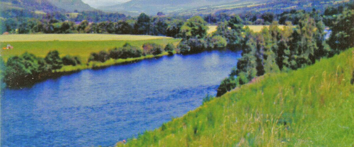 A river winding through a green landscape with hills in the background.