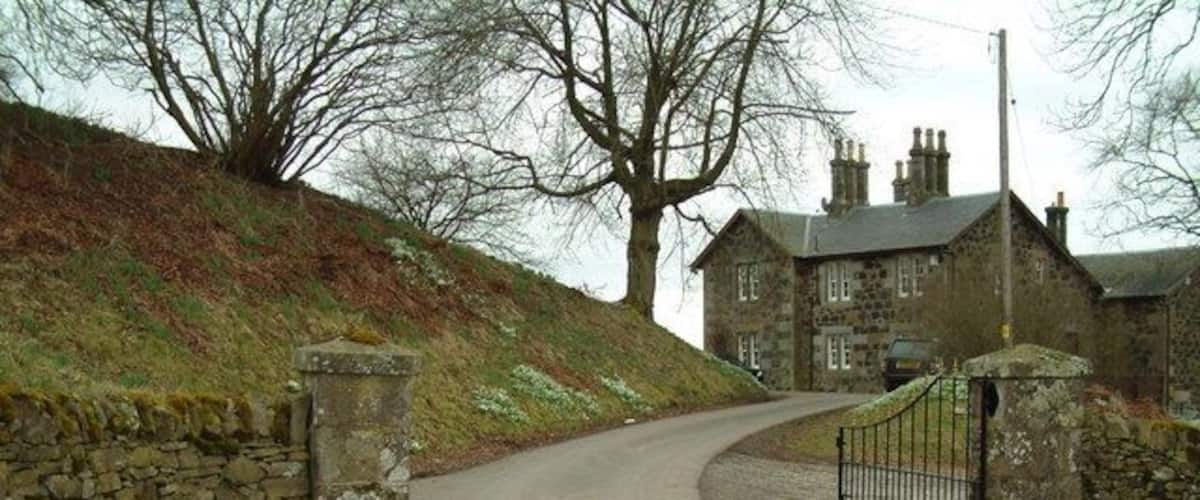 A rural road curving to a stone gate with a house in the background.
