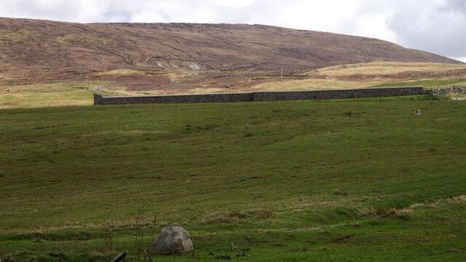 A stone wall in a grassy field with a hill in the background.