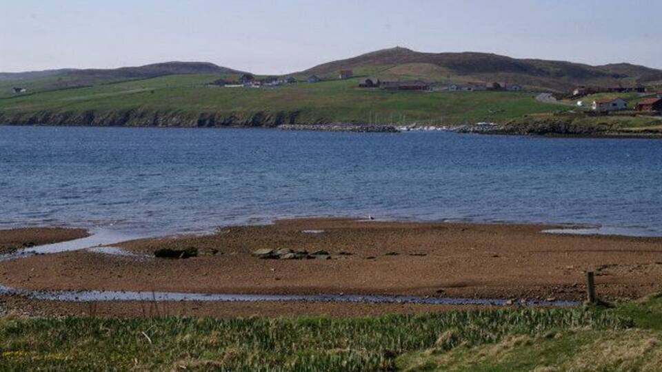A coastal landscape with a beach, grassy areas, and hills in the background.
