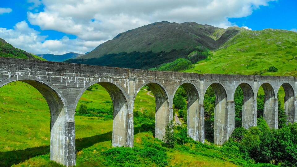 A stone viaduct with multiple arches over a lush green valley, with mountains in the background.