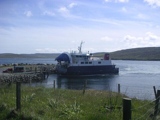Un ferry atracado en un muelle, con un césped al frente y colinas en el fondo.