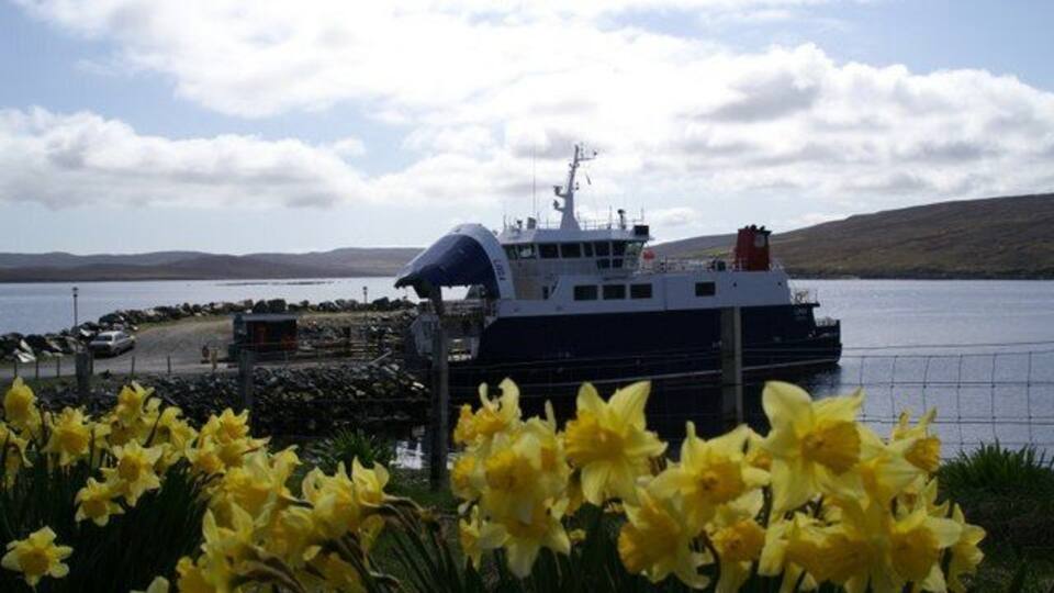 A ferry docked at a pier with a backdrop of a lake and hills.