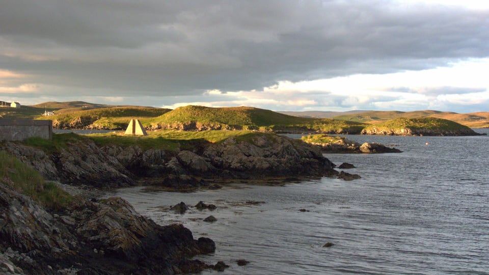 A coastal landscape with a lighthouse, rocky shore, and grassy hills.