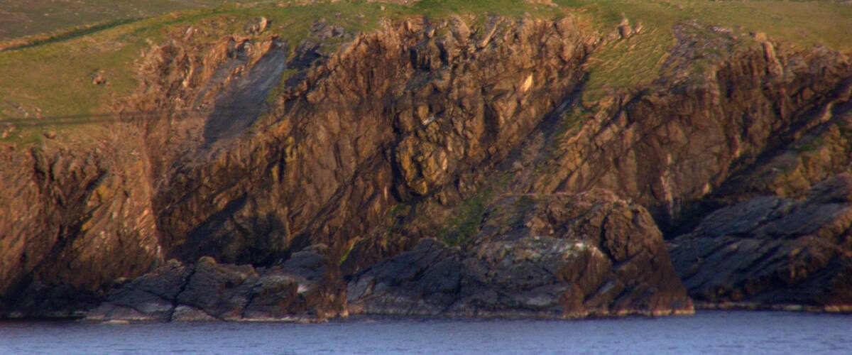 A small white tower on a grassy hill with rocky cliffs in the foreground.