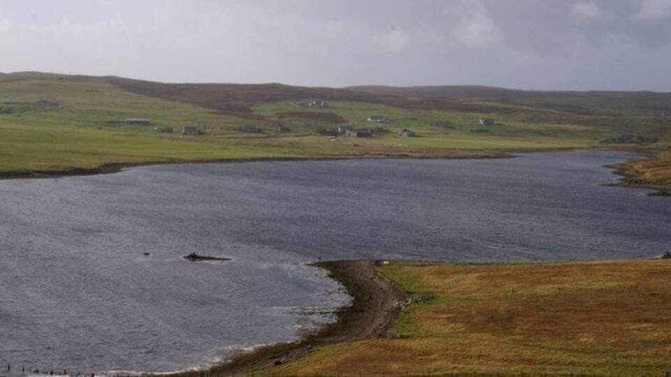 A coastal landscape with a body of water, grassy fields, and scattered houses.