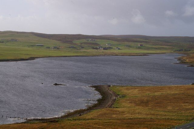 A coastal landscape with a body of water, grassy fields, and scattered houses.