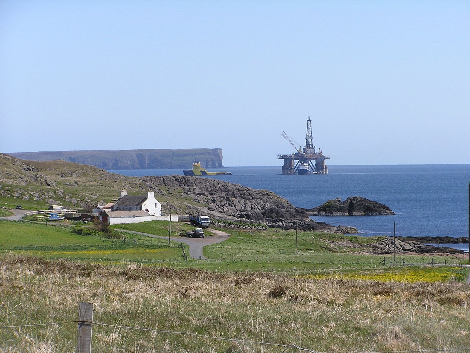A coastal landscape with a cliff, a small village, and an offshore oil rig.