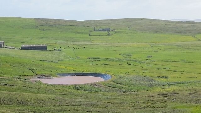Un paisaje verde con una estructura circular, un edificio y un área cercada.