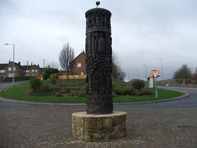 A decorative column with intricate carvings, a stop sign, and a residential area in the background.