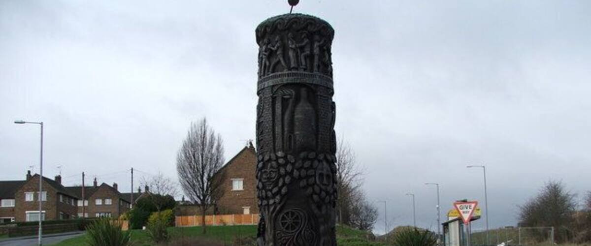 A decorative column with intricate carvings, a stop sign, and a residential area in the background.