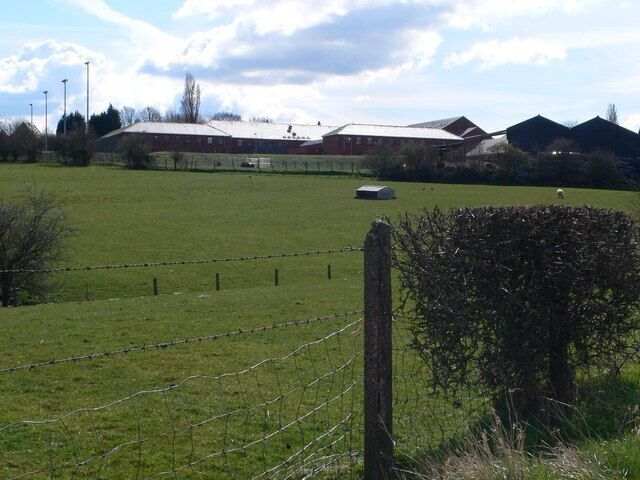 A rural landscape with a fenced field, a barn, and a few trees.