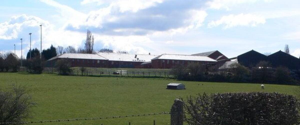 A rural landscape with a fenced field, a barn, and a few trees.