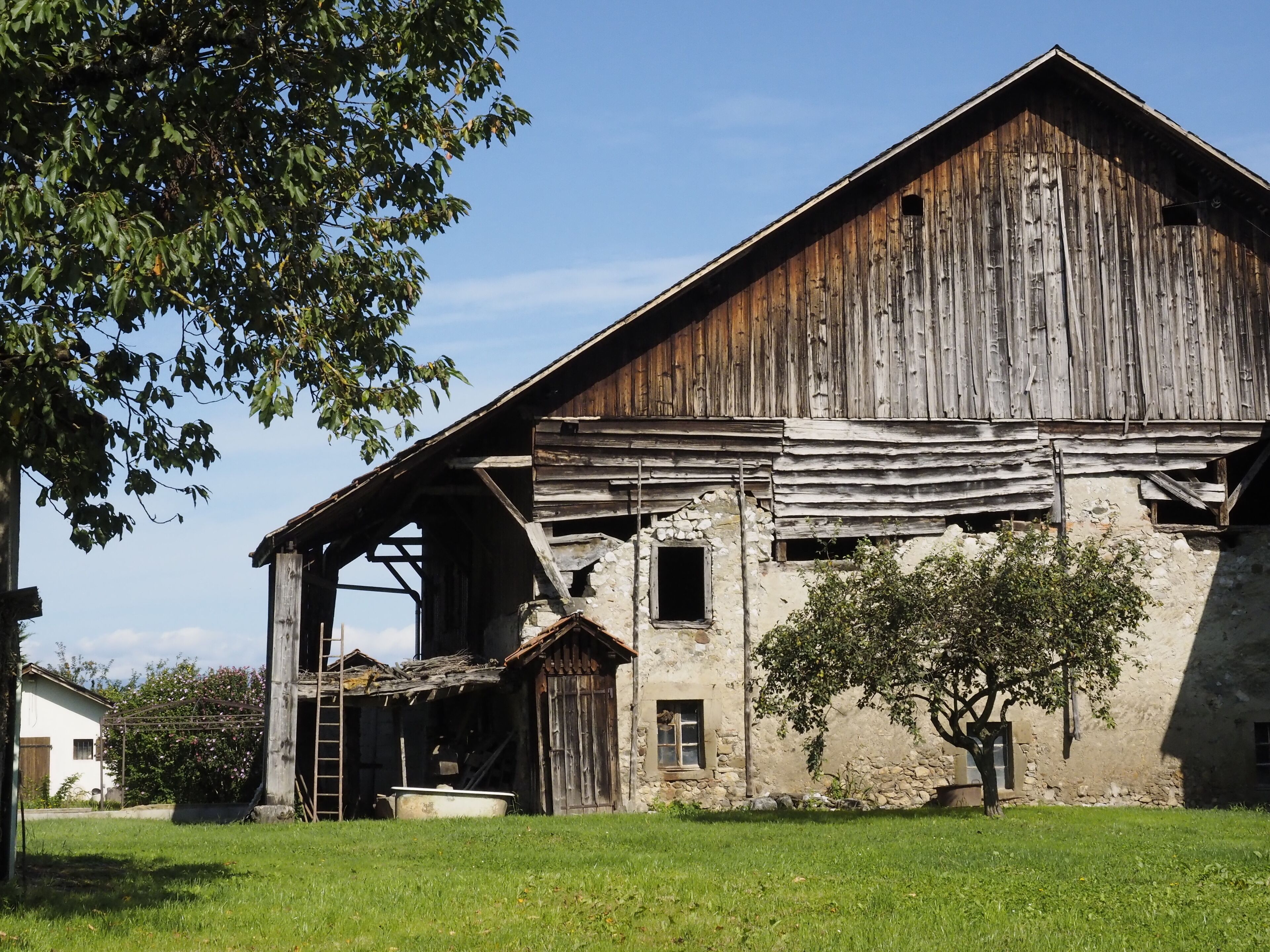 An old, weathered barn with a stone foundation, surrounded by a grassy field and trees.