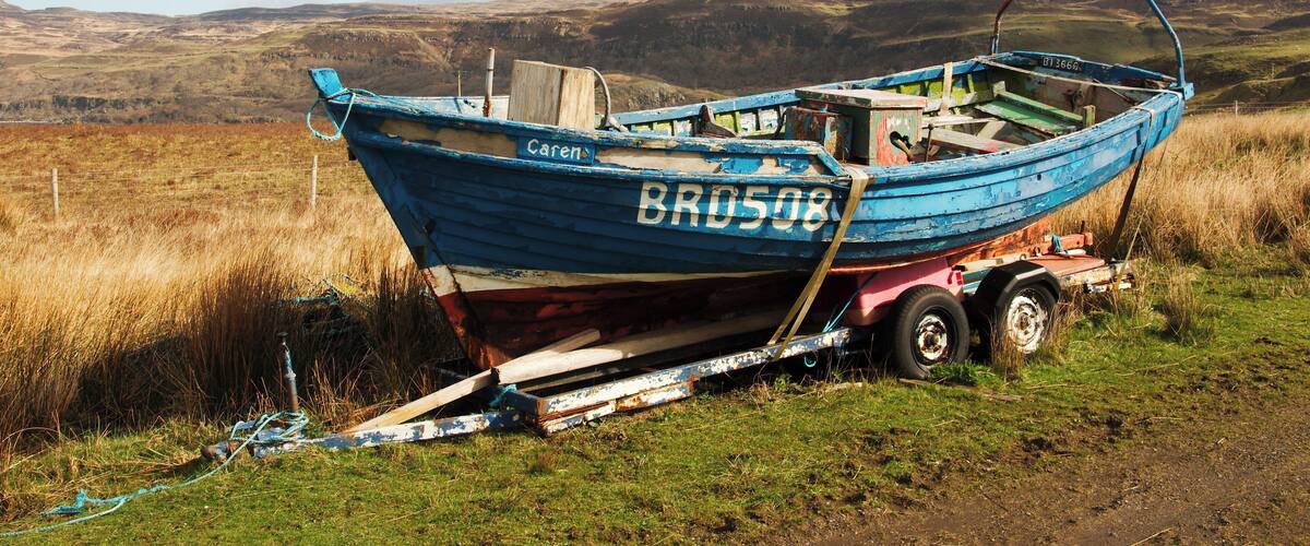 A blue boat named 'Bro508' with a trailer, parked on a grassy field with hills in the background.