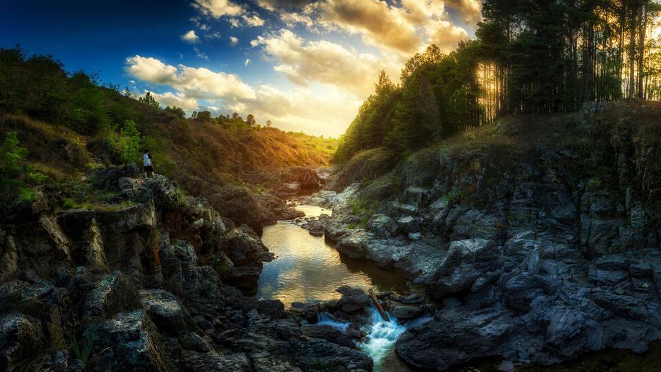 A river flowing through a rocky gorge with a person standing on a cliff.