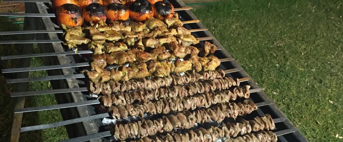 A barbecue grill with various meats and vegetables being cooked outdoors.