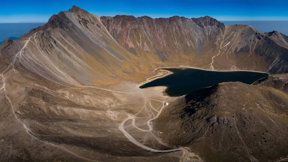 A mountainous landscape with a crater lake surrounded by rugged terrain.