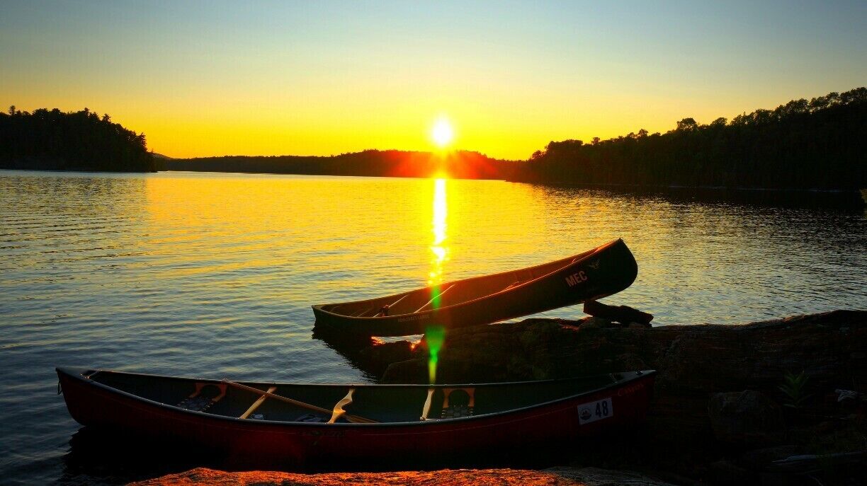 Two canoes on a calm lake at sunset with the sun reflecting on the water.