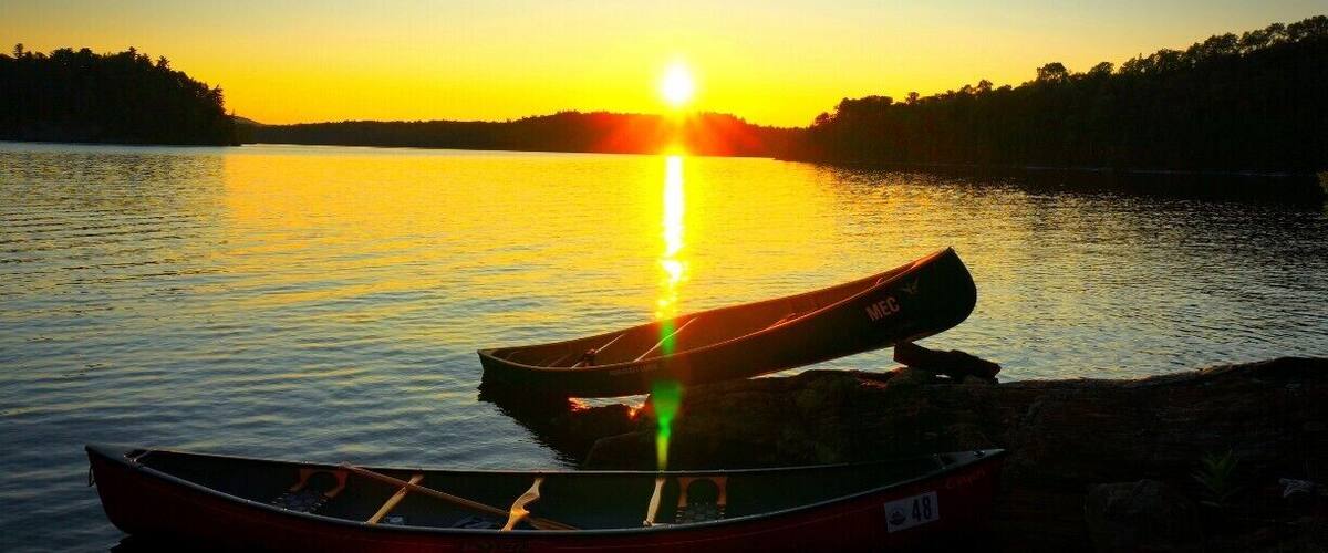 Two canoes on a calm lake at sunset with the sun reflecting on the water.