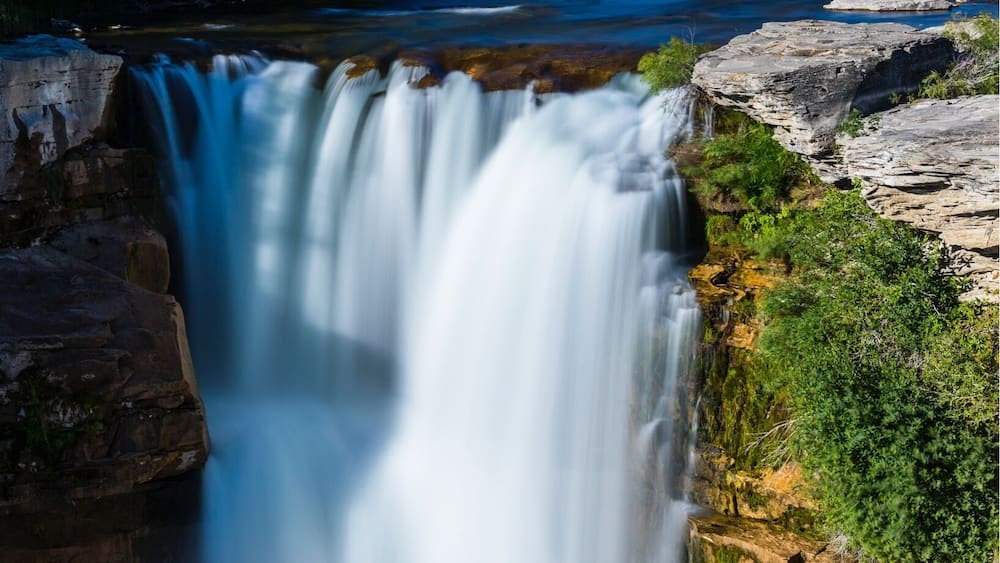 A waterfall, a river, and a bridge in a forested area.