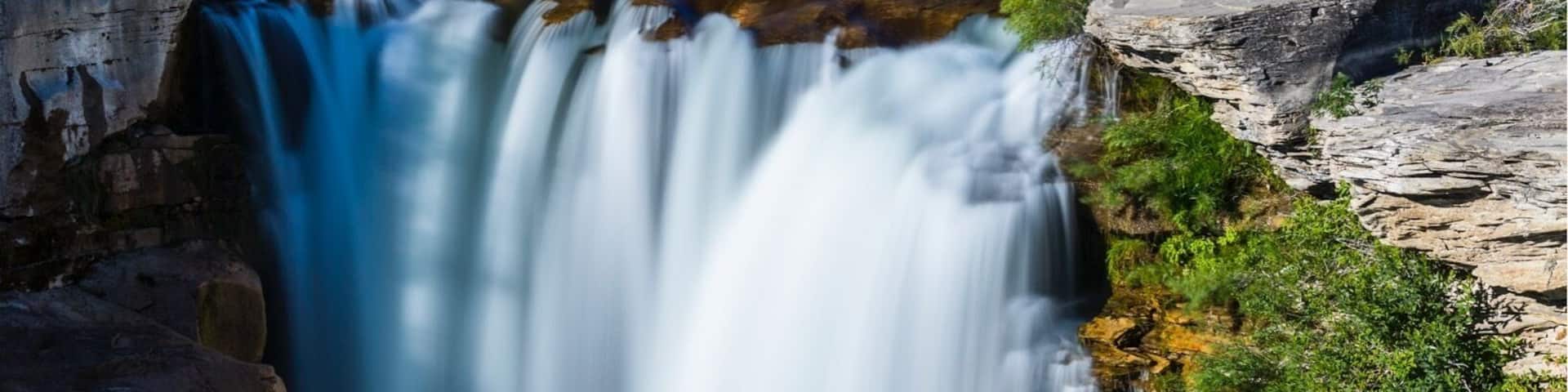 A waterfall, a river, and a bridge in a forested area.