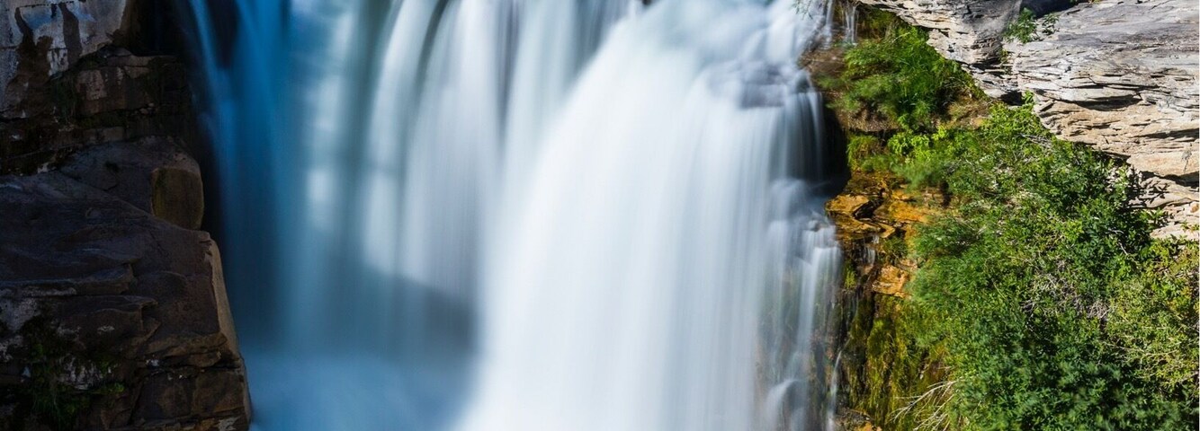 Uma cachoeira, um rio e uma ponte em uma área arborizada.
