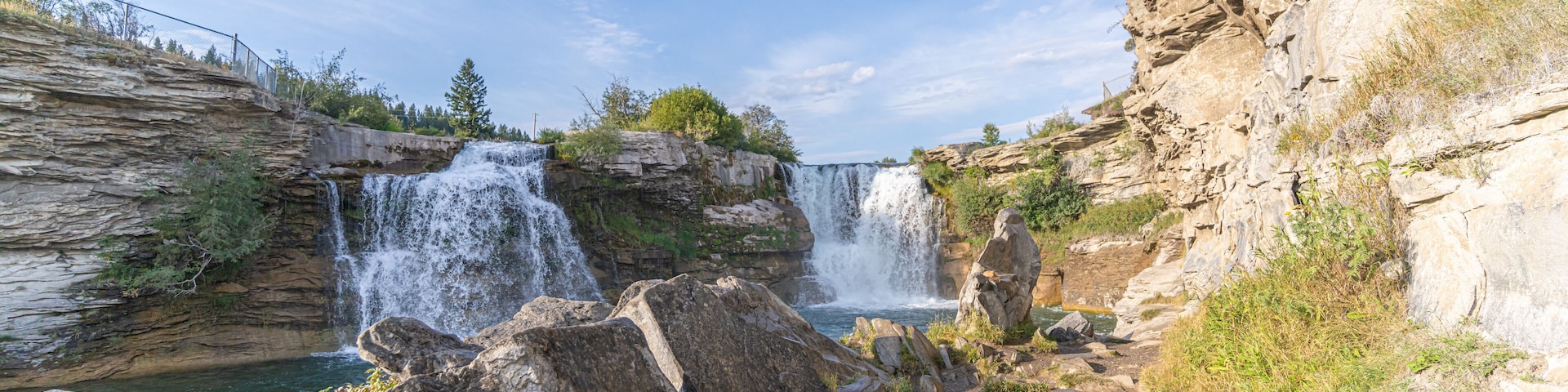 Una cascada se precipita sobre rocas hacia una poza, rodeada de acantilados y vegetación.