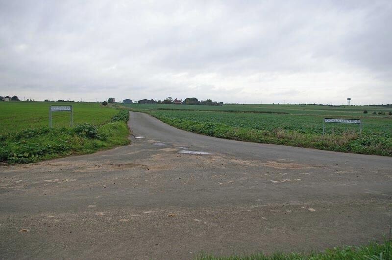 A rural road curving through fields with a water tower in the distance.