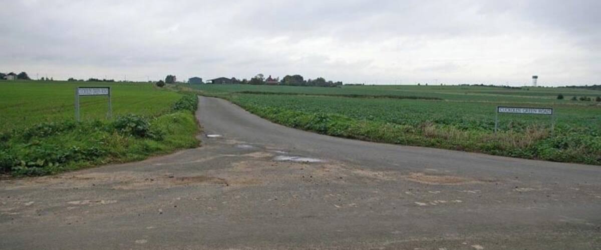 A rural road curving through fields with a water tower in the distance.